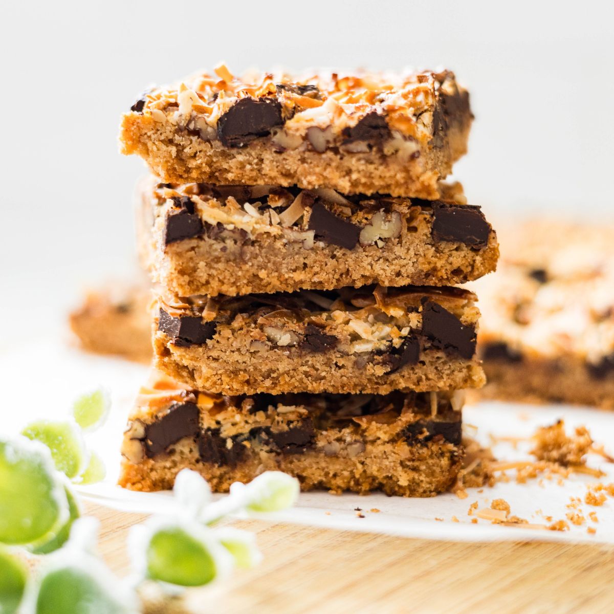 Stack of magic cookie bars showing the graham cracker crust, chocolate chips, pecans, and toasted coconut layers