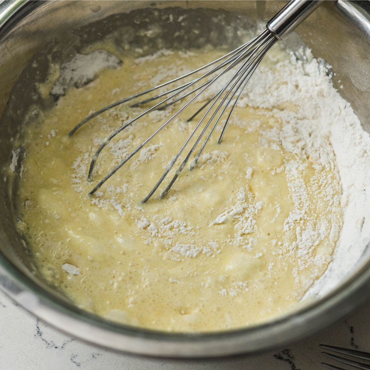 Mixing bibingka batter in a bowl with a whisk