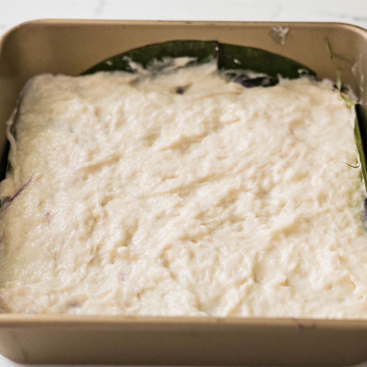 Plain coconut inutak layer spread in a banana leaf-lined baking dish