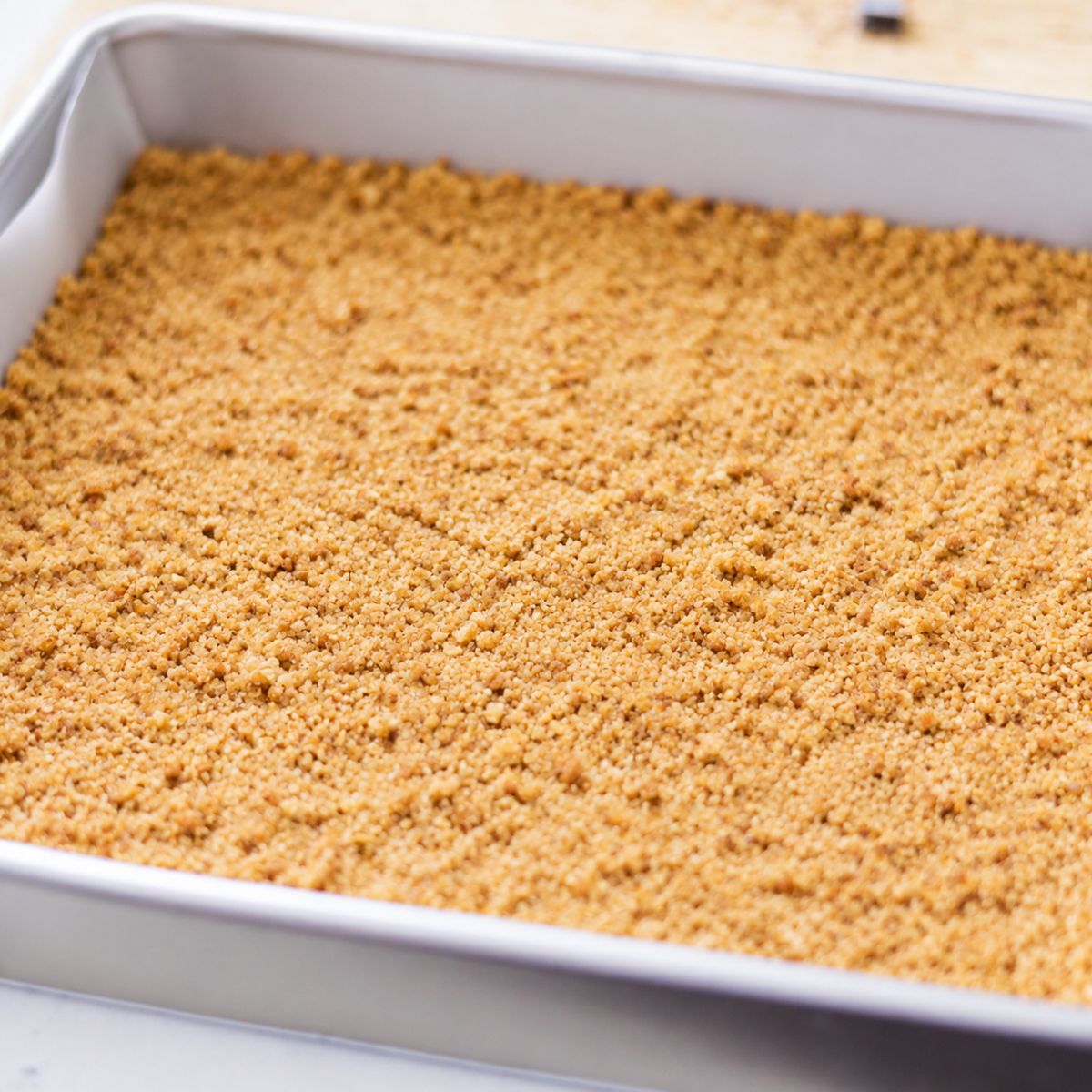Graham cracker crust pressed into an even layer in a square baking pan for magic cookie bars