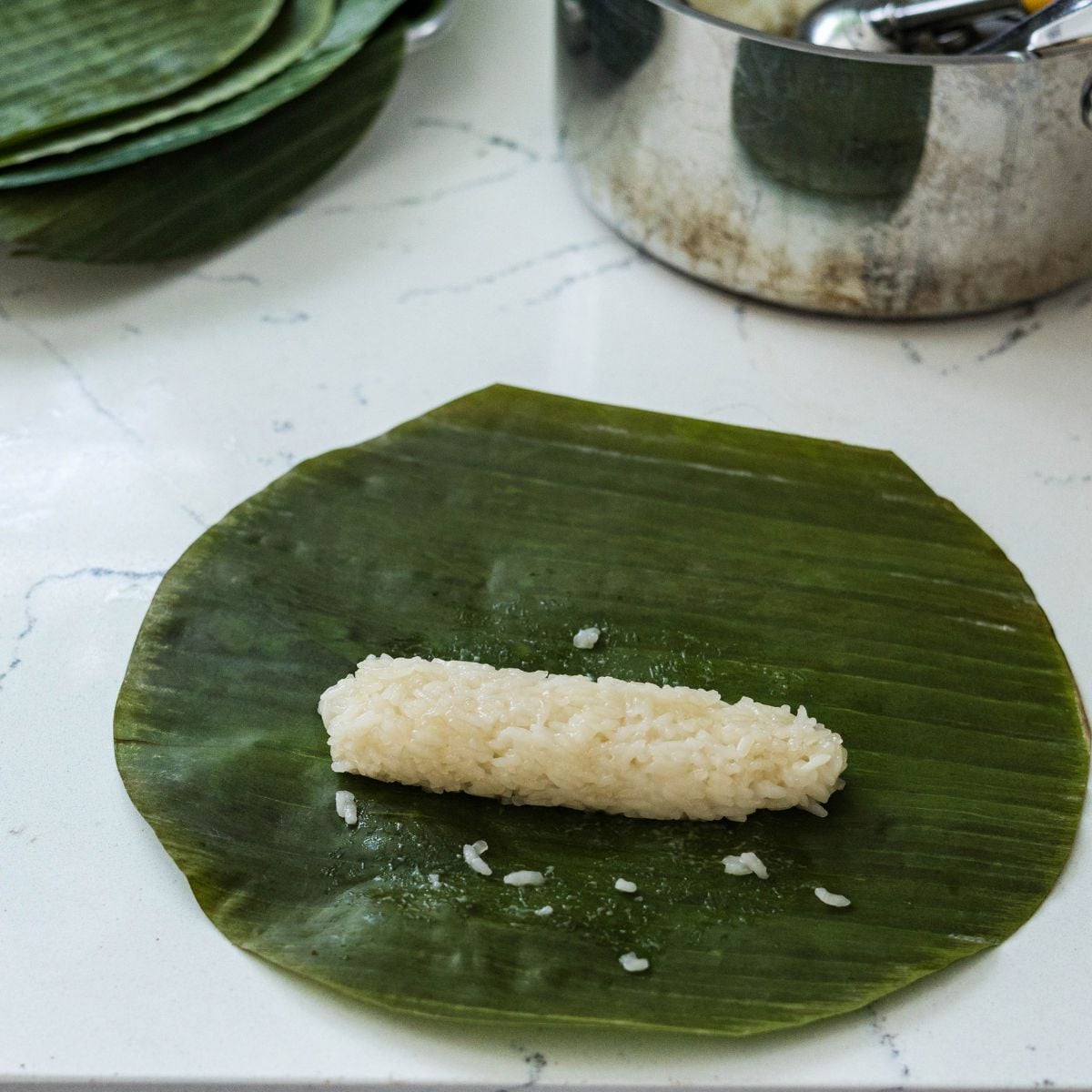 Sweet rice mixture being shaped and rolled in a banana leaf for suman