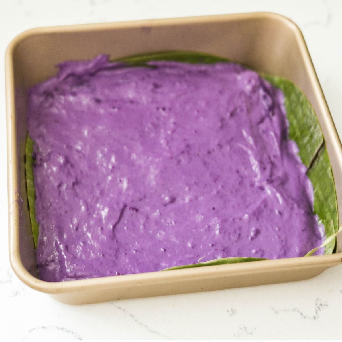 Purple ube inutak mixture spread evenly in a banana leaf-lined baking pan